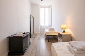 Et lille, rent værelse med seng, sengebord, lampe og skrivebord med stol.