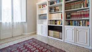 Una habitación con una amplia estantería llena de libros, una alfombra estampada y una puerta blanca.