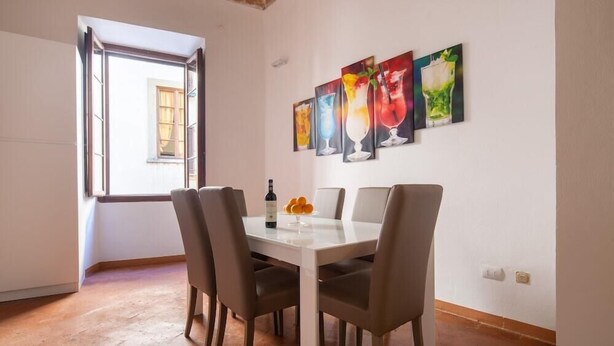 A dining area with a white table, four chairs, and a bottle of wine. There are four paintings on the wall depicting colorful drinks. - Lian Home in Florence (Florence)
