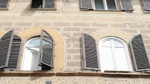A building with multiple arched windows with shutters, decorative brickwork, and a small statue in the lower window.