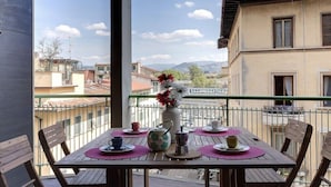 A balcony with a table set for tea, a vase with flowers, and a view of buildings and mountains. - Mamo Florence - Binario 9 Apartment (Florence)