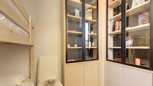 A compact room with a bunk bed, a small desk, and a built-in bookshelf with various items. - Mamo Florence - Binario 9 Apartment (Florence)