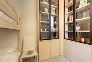 A compact room with a bunk bed, a small desk, and a built-in bookshelf with various items. - Mamo Florence - Binario 9 Apartment (Florence)