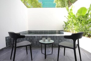 Un pequeño espacio al aire libre con dos sillas, una mesa, un muro de azulejos y algo de vegetación.