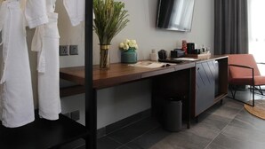 Una habitación de hotel moderna con un escritorio de madera, un televisor de pantalla plana, una silla roja y un perchero para bata.