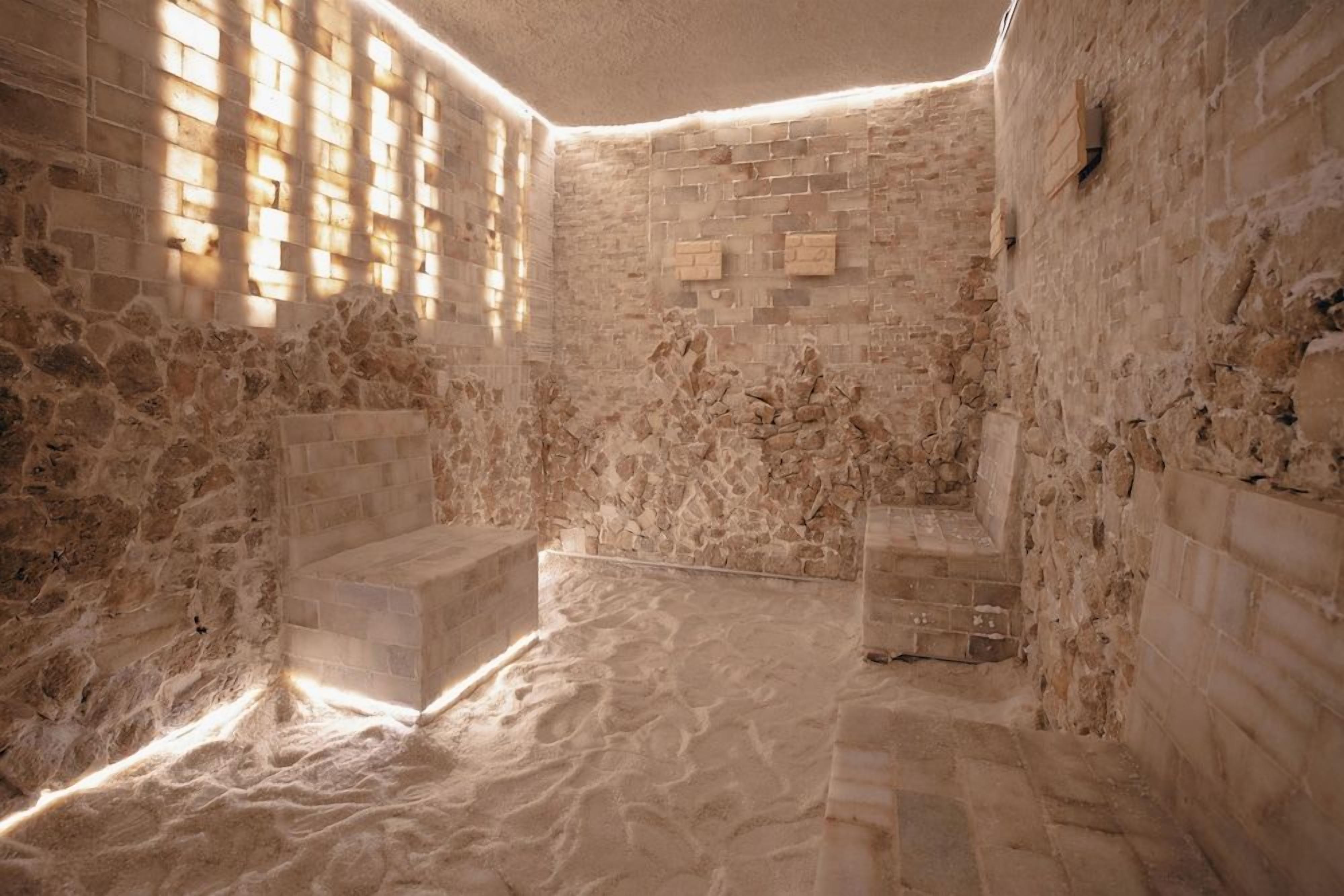 A stone-walled room with a sandy floor and a window allowing sunlight to enter.