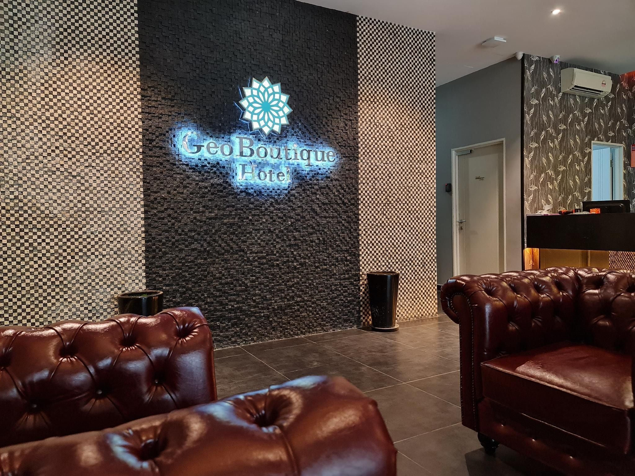 Eine Lobby mit einem 'Geo Boutique Hotel'-Schild, Ledersitzmöbeln und einer Wand mit Muster.