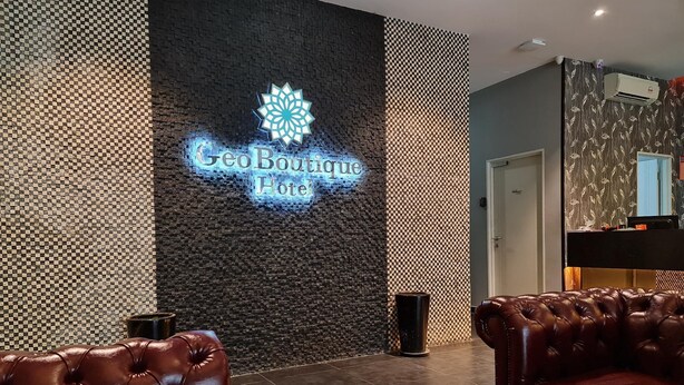 A lobby with a 'Geo Boutique Hotel' sign, leather seating, and a patterned wall. - Geo Boutique Hotel - Seri Kembangan (Seri Kembangan)