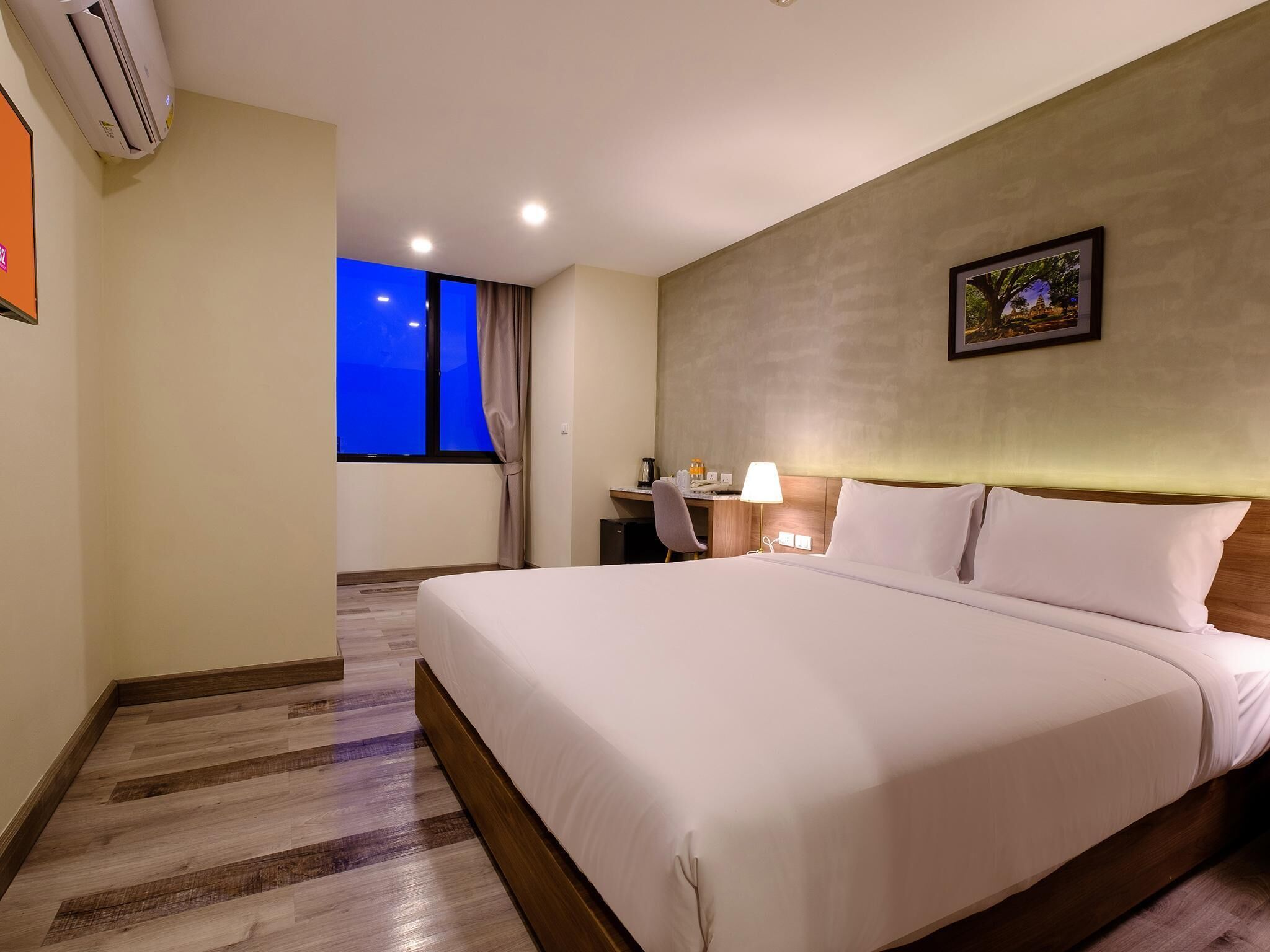 A hotel room with a large bed, a desk, a chair, a lamp, and a picture on the wall.