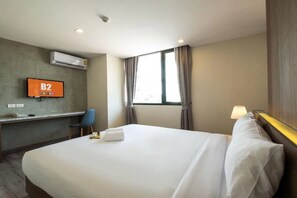 Una habitación de hotel con una cama grande, un escritorio con silla, televisor y ventana con cortinas.