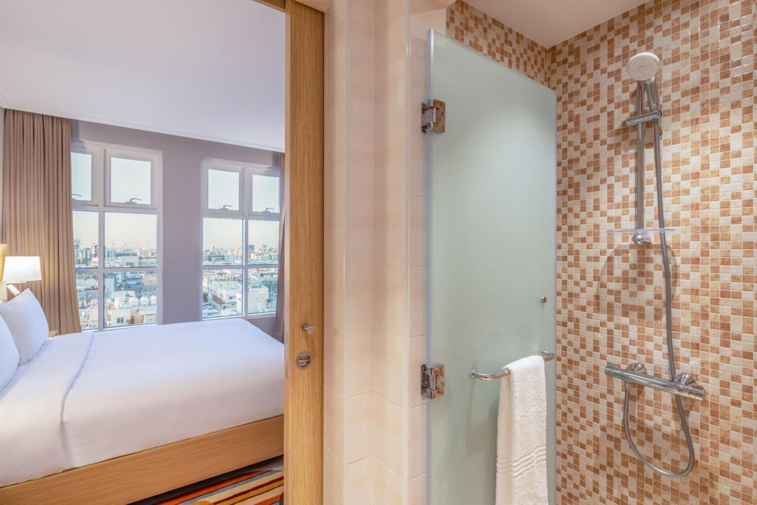 A hotel room with a bed, a shower, and a city view.