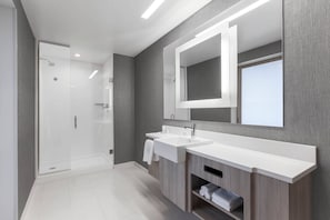 Un baño moderno con cabina de ducha de vidrio, un espejo grande y un lavabo con toallero.