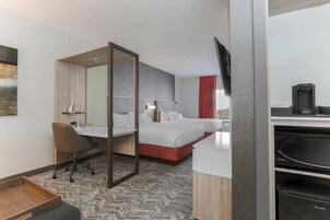 Quarto de hotel com cama, escrivaninha, cadeira, televisão e máquina de café.