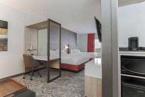 Habitación de hotel con cama, escritorio con silla, televisor, cafetera y microondas.
