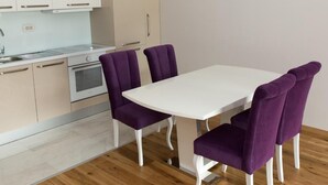A modern kitchen with white cabinets, a white dining table, and purple chairs. - Hotel Ponta Nova (Bečići)