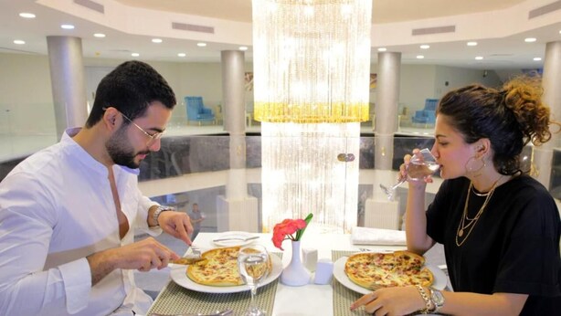 A dining area with a chandelier, a table with plates of food, and a vase with a flower. - Jewel Matrouh Hotel (Marsa Matrouh)