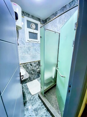 Un baño con suelo de mármol, cabina de ducha con vidrio, lavabo blanco y toallero.