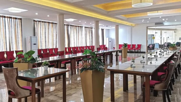 A spacious conference room with long tables, red chairs, and potted plants.