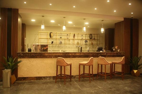 Un espace bar doté d’un comptoir en marbre, de trois tabourets de bar, d’un éclairage suspendu et d’une vitrine où sont exposés différents types de verres et de bouteilles.