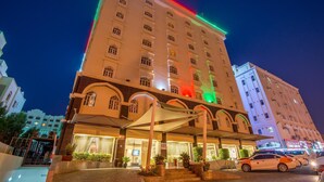 A multi-story hotel with a prominent entrance, a covered outdoor area, and a parking lot. - Caesar Hotel Oman (Muscat)