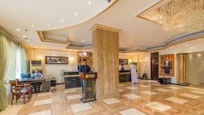 A hotel lobby with a reception desk, seating area, and a large chandelier. - Caesar Hotel Oman (Muscat)