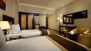 A hotel room with two beds, a desk, a chair, a TV, and a mirror. - Caesar Hotel Oman (Muscat)