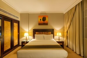 Habitación de hotel con una cama grande, dos mesitas de noche con lámparas, un cuadro en la pared y una ventana con cortinas.