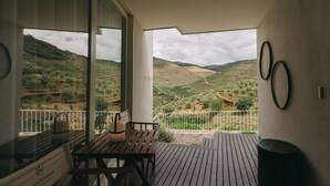 A balcony with a wooden table and chairs, a view of terraced vineyards, and a wall with circular decorations. - Ventozelo Hotel (São João da Pesqueira)