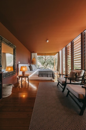 Un dormitorio con cama, mesitas de noche, una silla, un ventanal y vistas al exterior.