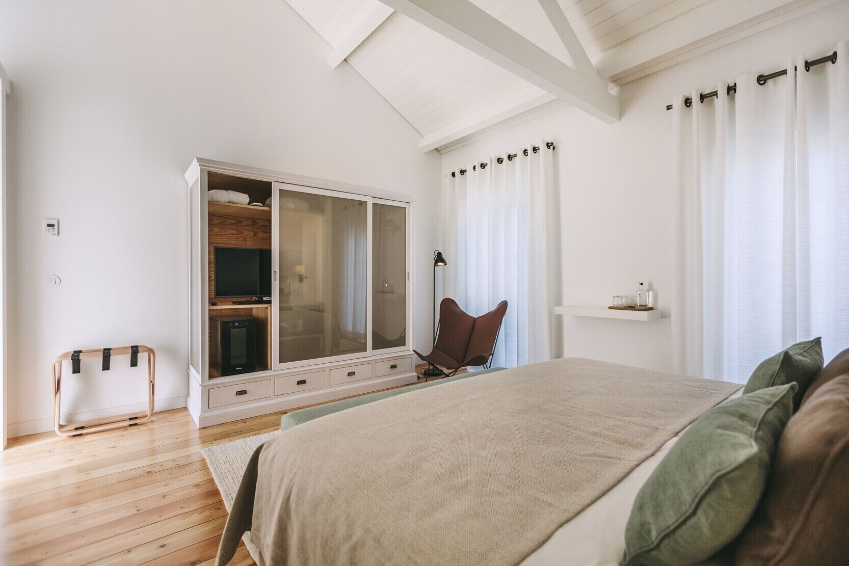 A bedroom with a large bed, a wardrobe, a chair, and a bedside table.