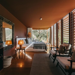Un dormitorio con cama, lámparas de noche, una silla, un espejo grande y vistas al exterior.