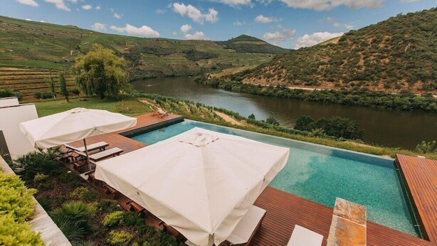 A pool area with wooden deck and lounge chairs, surrounded by lush greenery and a view of a river and hills. - Ventozelo Hotel (São João da Pesqueira)