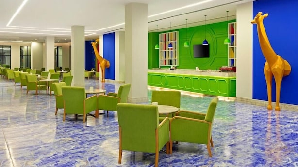 A modern hotel lobby with green chairs, a reception desk, and a giraffe statue.