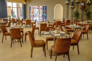 Un vaste espace dédié à la salle à manger, avec de nombreuses tables et chaises, de grandes fenêtres et un vitrail aux couleurs vives.