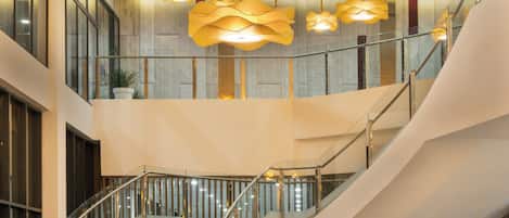 A modern interior with a central staircase, a reception desk labeled 'Concierge', and multiple hanging light fixtures.