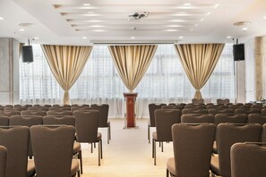 A conference room with rows of chairs, a podium, and large windows with curtains.