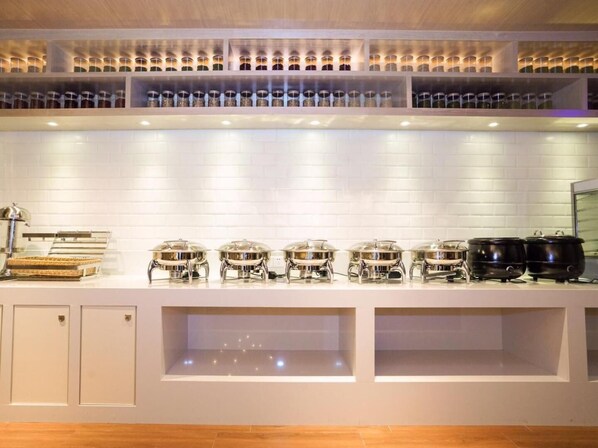 A buffet setup with multiple serving stations, a glass display case, and a white tiled backsplash. - Echarm Hotel (Guangzhou)