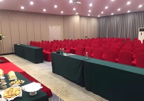 Ein Konferenzraum mit roten Stühlen, einem grünen Tisch und einem Projektor sowie einem weißen Teppich.