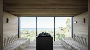 Un sauna doté de bancs et d’un élément décoratif central en pierre, ainsi que de grandes fenêtres offrant une vue sur l’extérieur.
