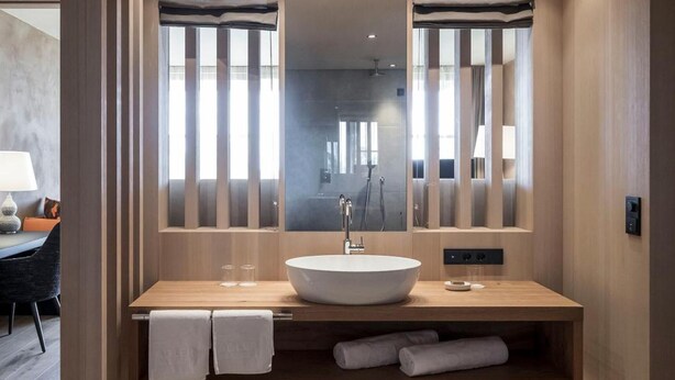 Un baño moderno con un espejo grande, un lavamanos redondo y una ducha. Hay toallas en la encimera y un banco debajo.