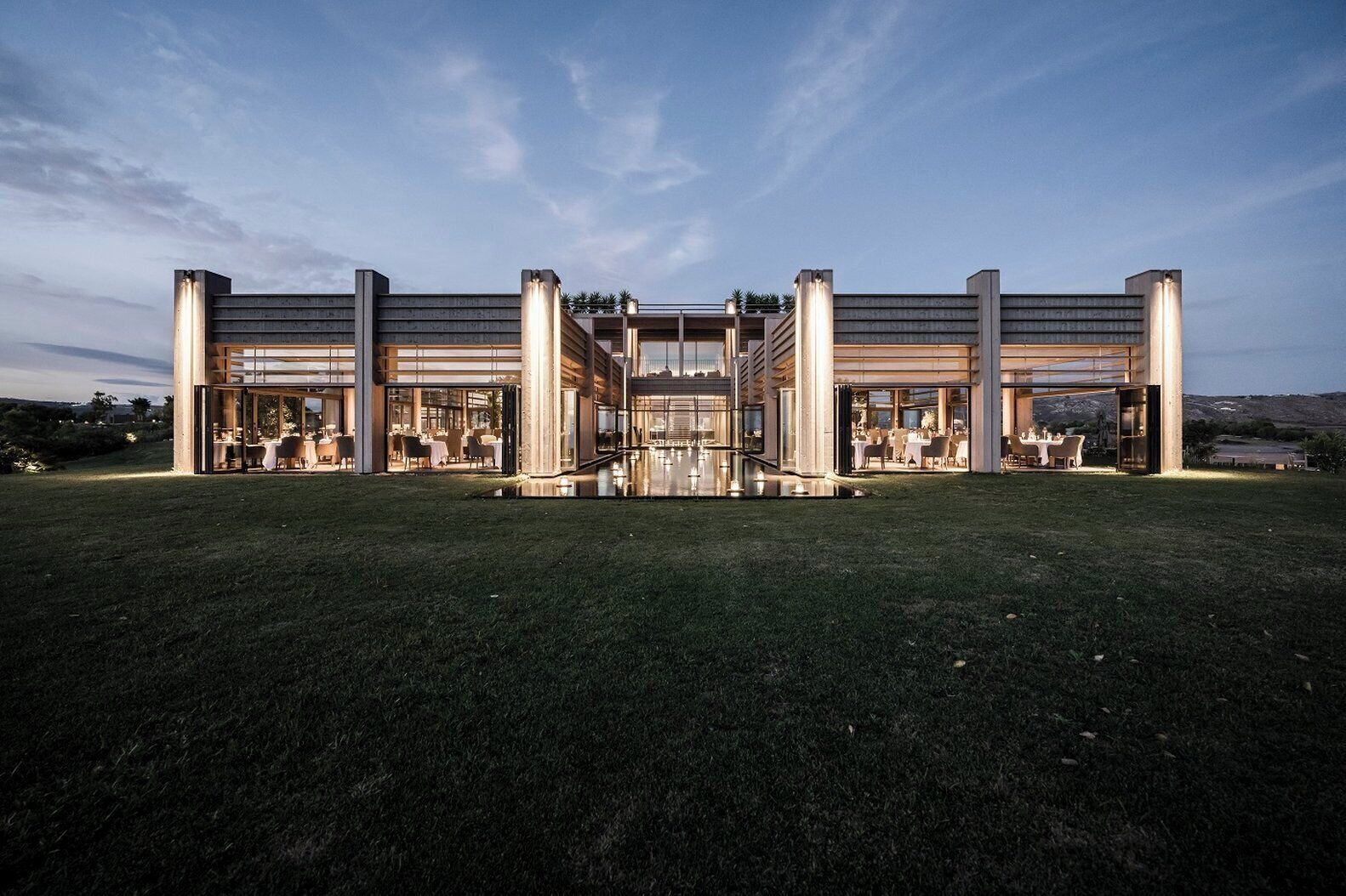 Un edificio moderno con ampie vetrate, un atrio centrale e aree salotto all'aperto.