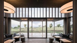 Un intérieur moderne avec une grande porte vitrée donnant sur un espace extérieur, un plancher en bois et différents espaces aménagés pour s’asseoir.