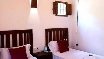 A room with two beds, wooden headboards, a small window, and a hanging light fixture.