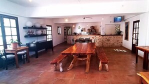 A spacious dining area with a large wooden table and benches, a kitchen area with a stone counter, and a television mounted on the wall. - Sa Pergola (Formentera)
