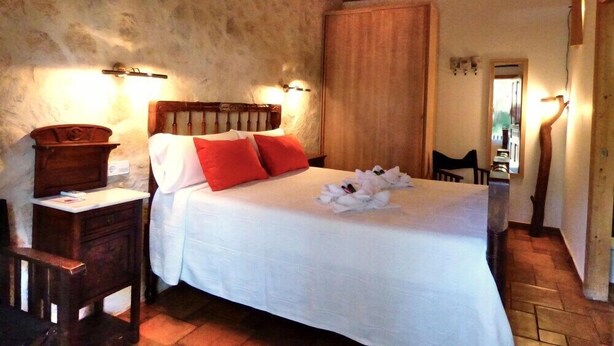 A bedroom with a wooden headboard, a white bedspread, red pillows, and a wooden nightstand with a lamp. - Sa Pergola (Formentera)