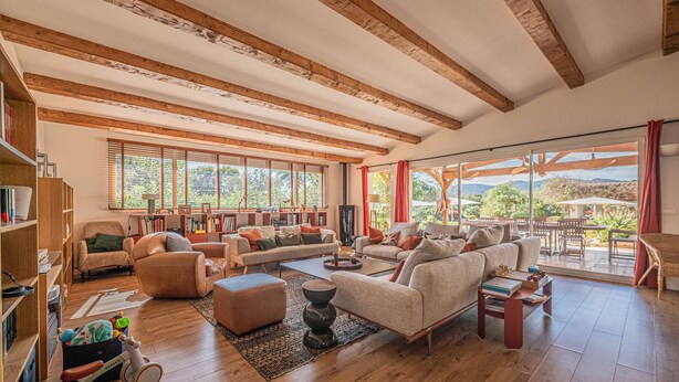 A spacious living room with wooden beams, large windows, a sofa set, a coffee table, and a bookshelf. - Grimaud amazing villa with a swiming pool (GRIMAUD)