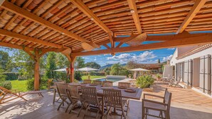 An outdoor patio with a wooden pergola, a dining table with chairs, and a view of a swimming pool and greenery. - Grimaud amazing villa with a swiming pool (GRIMAUD)
