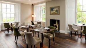 Un comedor con mesas y sillas de madera, ventanas amplias y una chimenea.