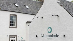 Un edificio blanco con chimenea, una puerta y una ventana. El edificio tiene un letrero que dice 'Marmalade Hotel'.