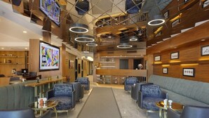 En moderne lobby med en central receptionsdisk, siddeområde med sofaer og lænestole, samt en trappe med trægelændere.